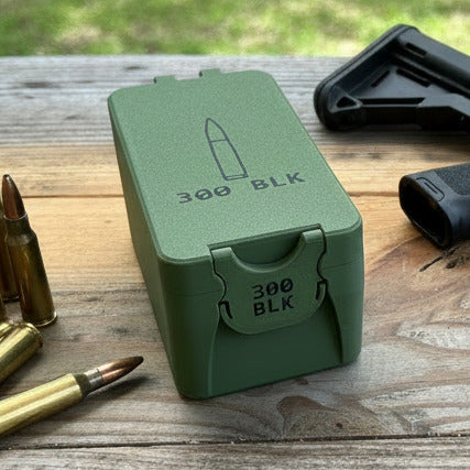 Green ammunition box labeled '300 BLK' on a wooden surface with grass in the background